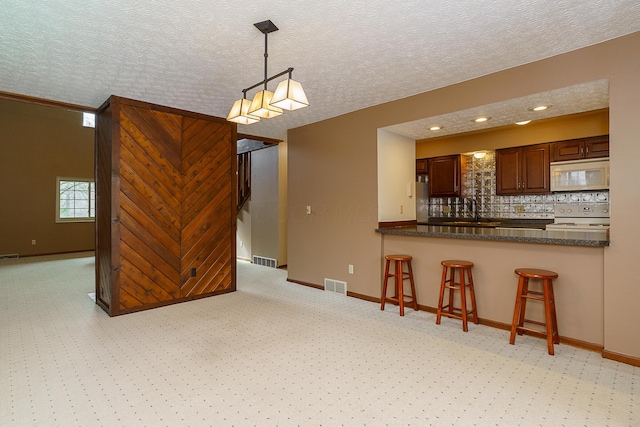 kitchen with decorative light fixtures, dark countertops, visible vents, white appliances, and a peninsula