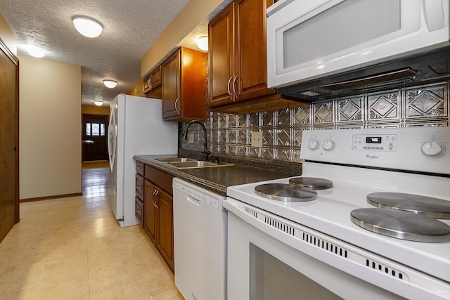 kitchen with light floors, dark countertops, a sink, a textured ceiling, and white appliances