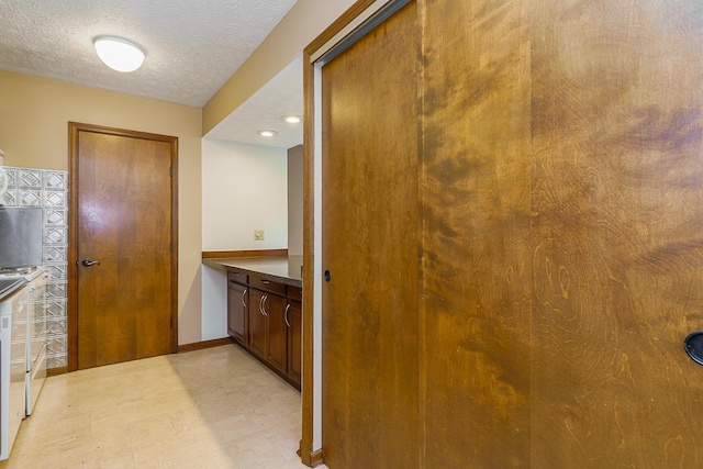 corridor with light floors, baseboards, and a textured ceiling