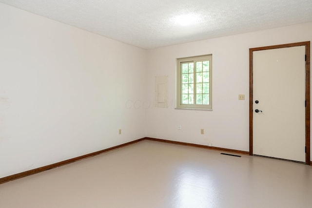 spare room with visible vents, a textured ceiling, electric panel, concrete floors, and baseboards