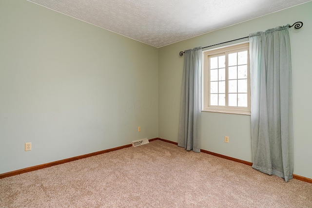 unfurnished room with light carpet, visible vents, baseboards, and a textured ceiling