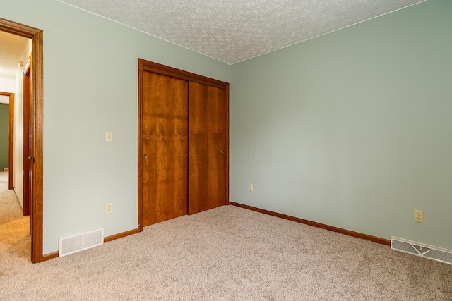 unfurnished bedroom with a textured ceiling, visible vents, a closet, and light colored carpet