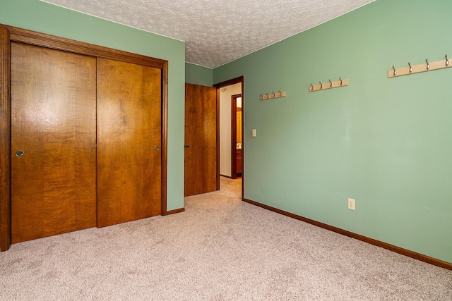 unfurnished bedroom with a textured ceiling, baseboards, a closet, and light colored carpet