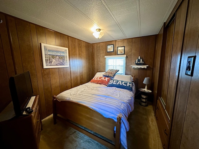 bedroom with wood walls, a textured ceiling, and dark colored carpet