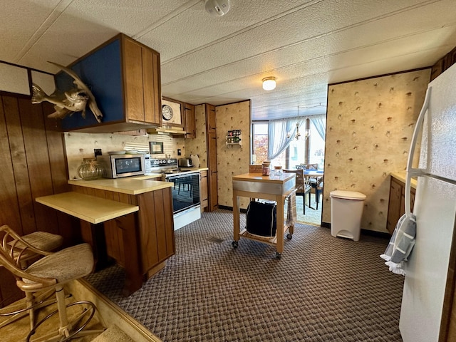 kitchen with hanging light fixtures, dark colored carpet, white electric range, kitchen peninsula, and wood walls