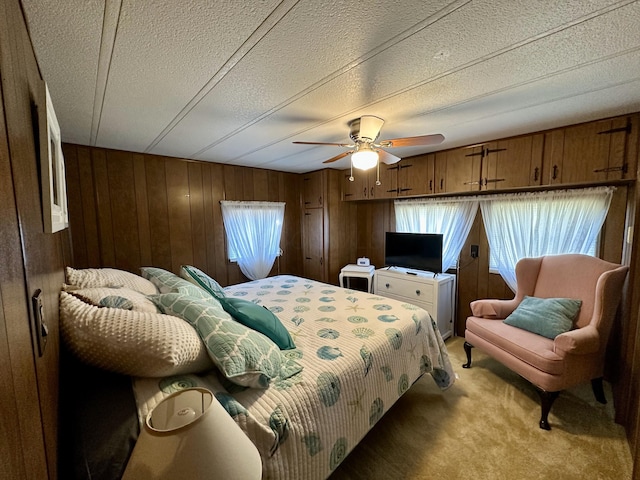 carpeted bedroom with ceiling fan, wood walls, and a textured ceiling