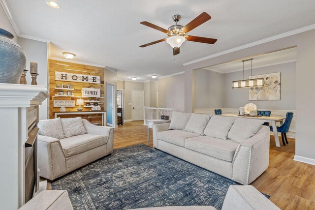 living room featuring wooden walls, light hardwood / wood-style flooring, ceiling fan, and crown molding