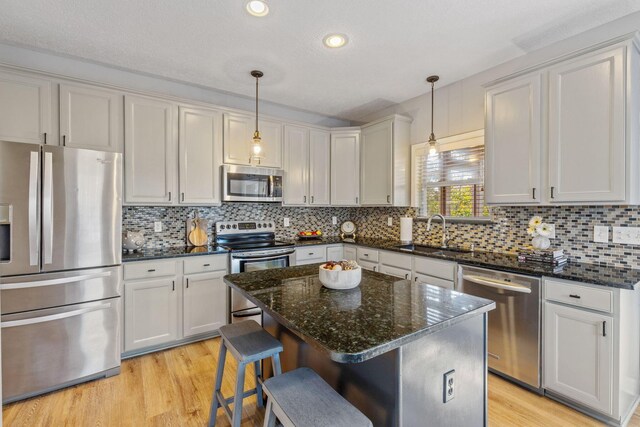 kitchen with a center island, sink, appliances with stainless steel finishes, decorative light fixtures, and a breakfast bar area