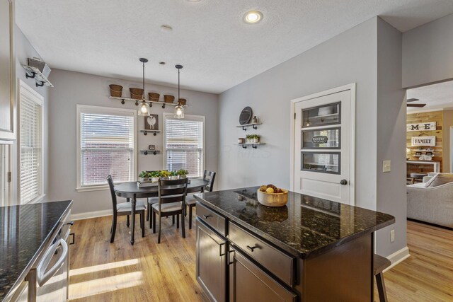 kitchen with pendant lighting, light hardwood / wood-style floors, a textured ceiling, and dark stone counters