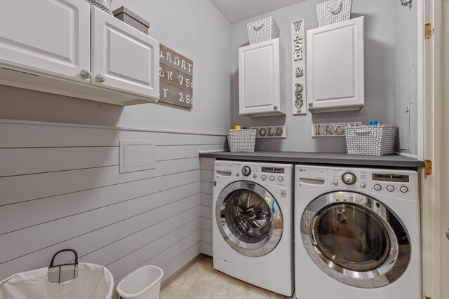 clothes washing area featuring cabinets, wooden walls, and washing machine and clothes dryer