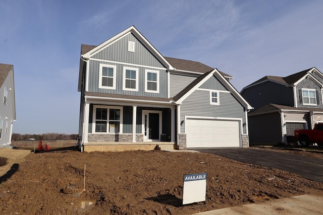 craftsman-style house with roof with shingles, covered porch, board and batten siding, stone siding, and driveway