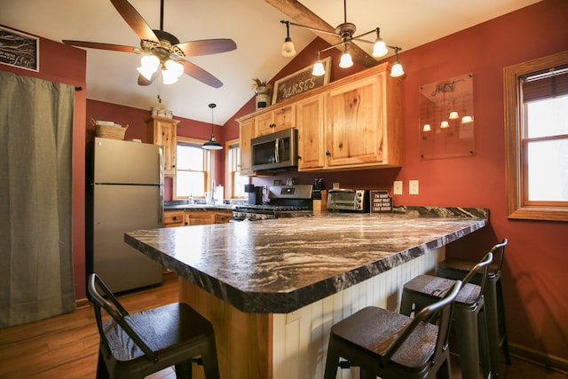 kitchen with pendant lighting, lofted ceiling, appliances with stainless steel finishes, a kitchen bar, and kitchen peninsula