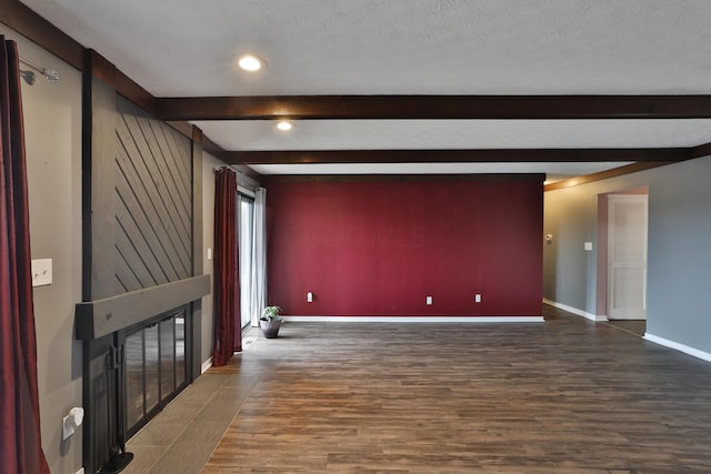 spare room featuring beamed ceiling, dark wood-type flooring, and a textured ceiling