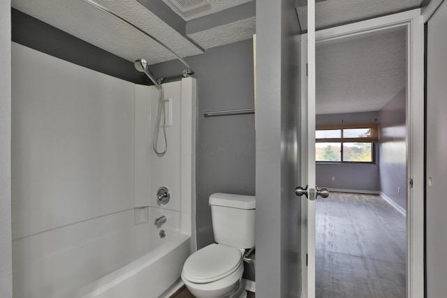 bathroom featuring wood-type flooring, a textured ceiling, toilet, and tub / shower combination