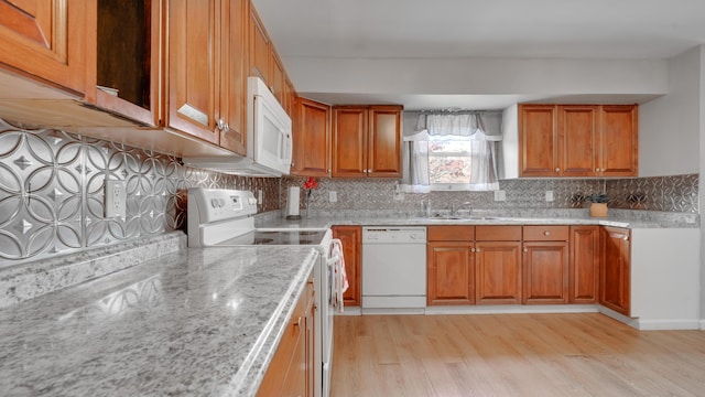 kitchen featuring light stone countertops, sink, backsplash, white appliances, and light wood-type flooring