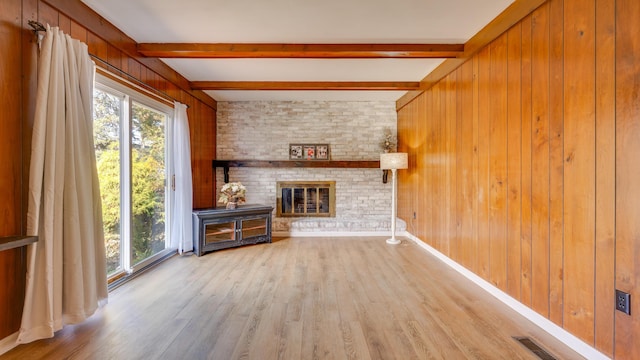 unfurnished living room with beamed ceiling, light hardwood / wood-style floors, a brick fireplace, and wood walls