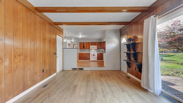 unfurnished living room with wood walls, beamed ceiling, and light hardwood / wood-style floors