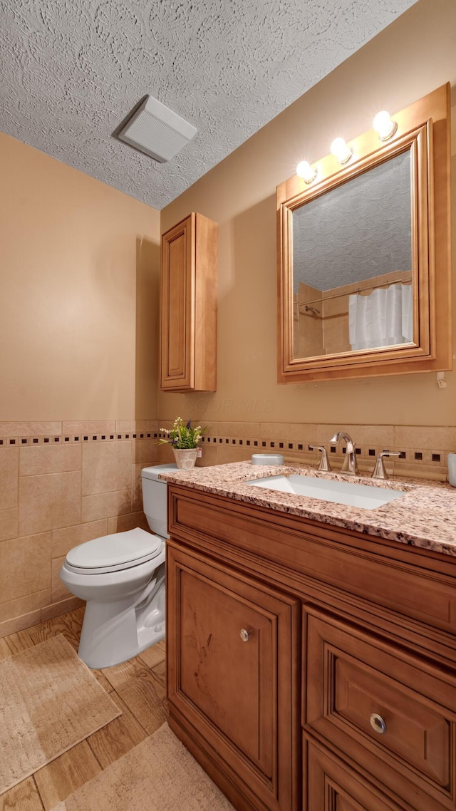 bathroom featuring vanity, hardwood / wood-style flooring, toilet, a textured ceiling, and tile walls