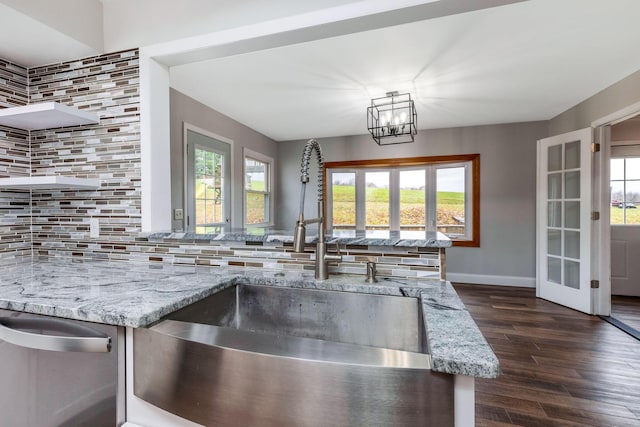 kitchen with light stone countertops, dark hardwood / wood-style flooring, tasteful backsplash, sink, and an inviting chandelier