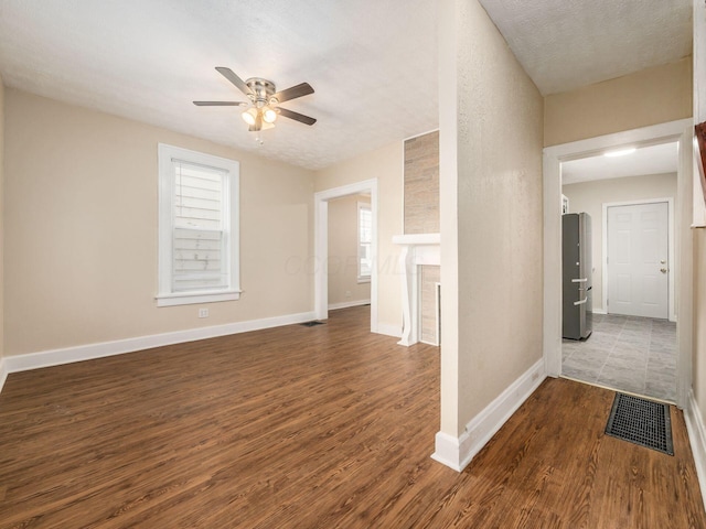 interior space with a textured ceiling, ceiling fan, a large fireplace, and dark hardwood / wood-style floors