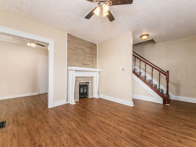 unfurnished living room featuring a textured ceiling, ceiling fan, a fireplace, and dark wood-type flooring