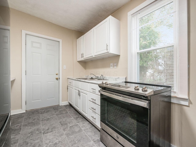 kitchen featuring stainless steel electric stove, a wealth of natural light, and white cabinets