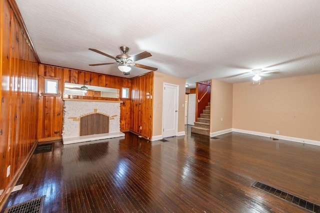 unfurnished living room with wooden walls, dark hardwood / wood-style floors, ceiling fan, a textured ceiling, and a fireplace