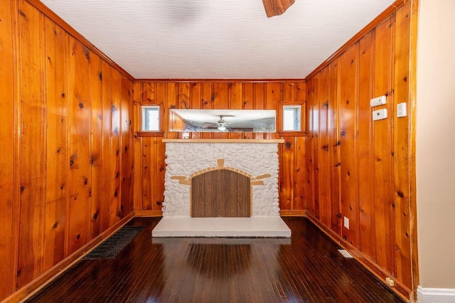 unfurnished living room featuring ceiling fan, wood walls, dark hardwood / wood-style flooring, and a fireplace