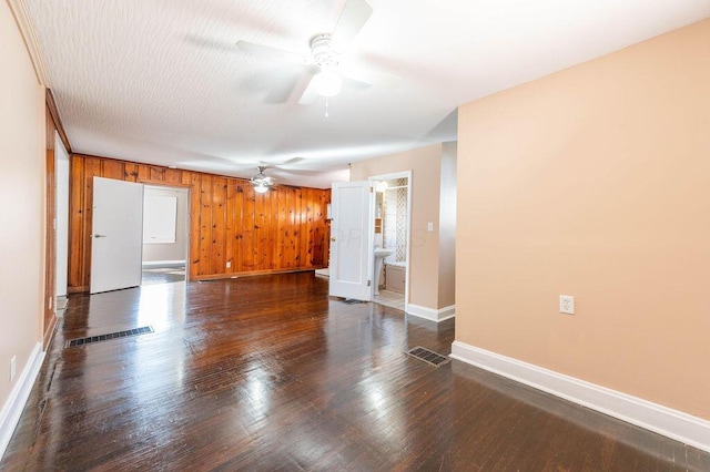 spare room featuring ceiling fan, dark hardwood / wood-style flooring, and wooden walls