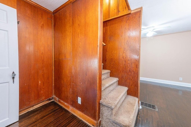 staircase featuring hardwood / wood-style flooring, ceiling fan, and wooden walls