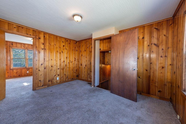 unfurnished bedroom with carpet floors, a closet, and wood walls