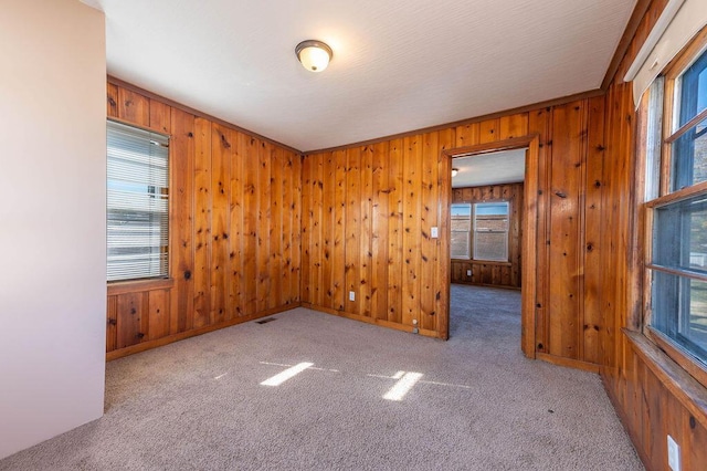 carpeted spare room featuring crown molding, a healthy amount of sunlight, and wood walls