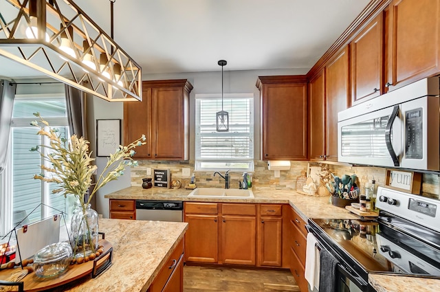 kitchen with light stone countertops, sink, hanging light fixtures, backsplash, and appliances with stainless steel finishes