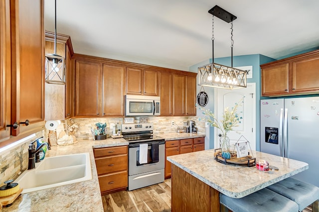 kitchen with sink, light wood-type flooring, appliances with stainless steel finishes, decorative light fixtures, and a breakfast bar area