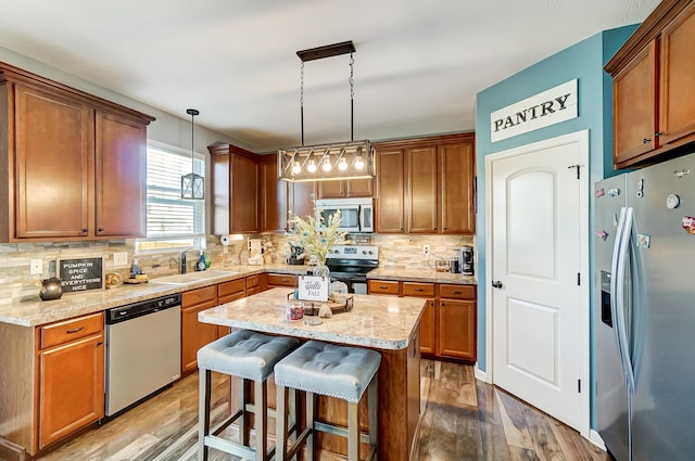 kitchen with sink, appliances with stainless steel finishes, decorative light fixtures, a kitchen bar, and wood-type flooring