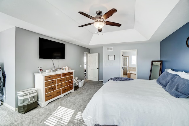 carpeted bedroom featuring a tray ceiling, ensuite bath, and ceiling fan