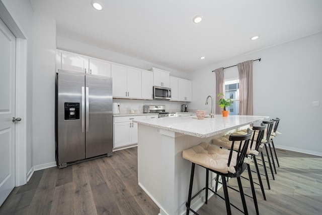 kitchen with white cabinets, a breakfast bar, a kitchen island with sink, and appliances with stainless steel finishes