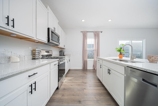 kitchen featuring light stone countertops, appliances with stainless steel finishes, sink, white cabinets, and hardwood / wood-style floors