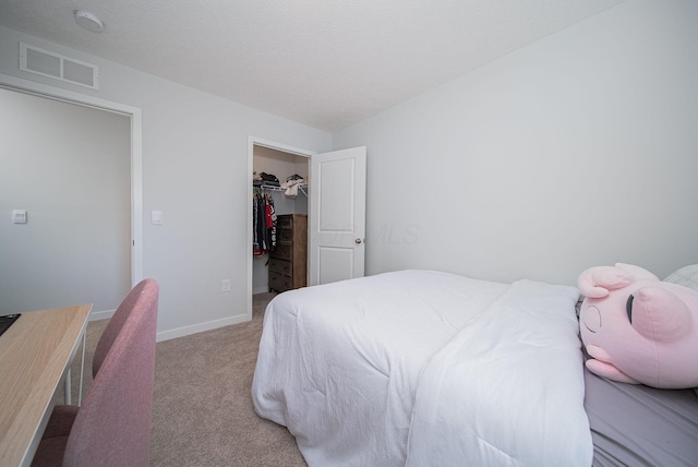 bedroom with light carpet, a textured ceiling, a walk in closet, and a closet