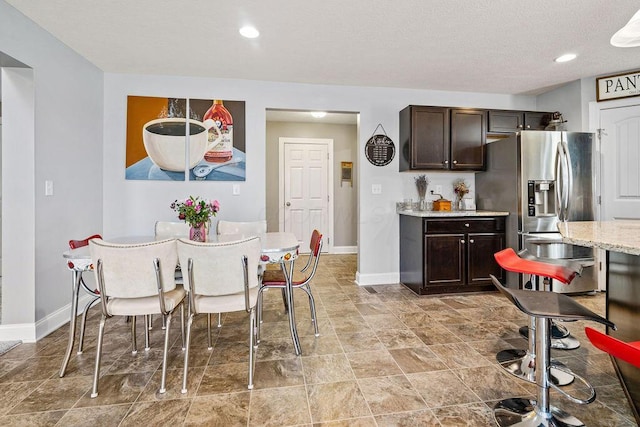 kitchen featuring light stone countertops, baseboards, recessed lighting, dark brown cabinets, and stainless steel refrigerator with ice dispenser