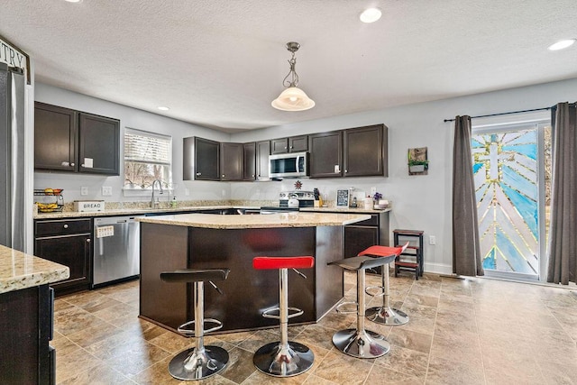 kitchen featuring a breakfast bar area, a sink, hanging light fixtures, stainless steel appliances, and a center island