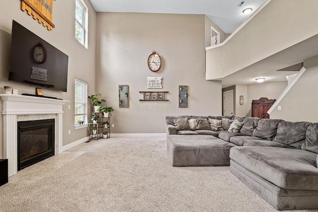 carpeted living room featuring a high end fireplace, baseboards, and a towering ceiling