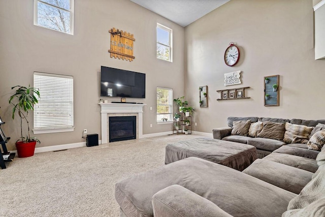 carpeted living area with a glass covered fireplace, visible vents, baseboards, and a towering ceiling