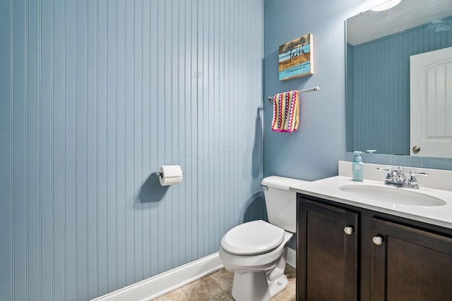 half bath with baseboards, toilet, and vanity