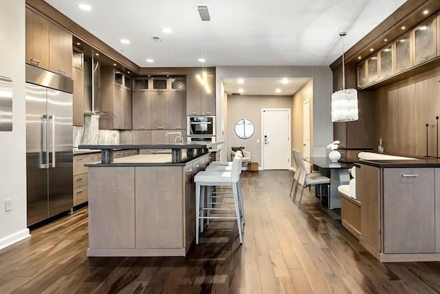 kitchen with a center island, dark wood-type flooring, hanging light fixtures, wall chimney range hood, and built in refrigerator