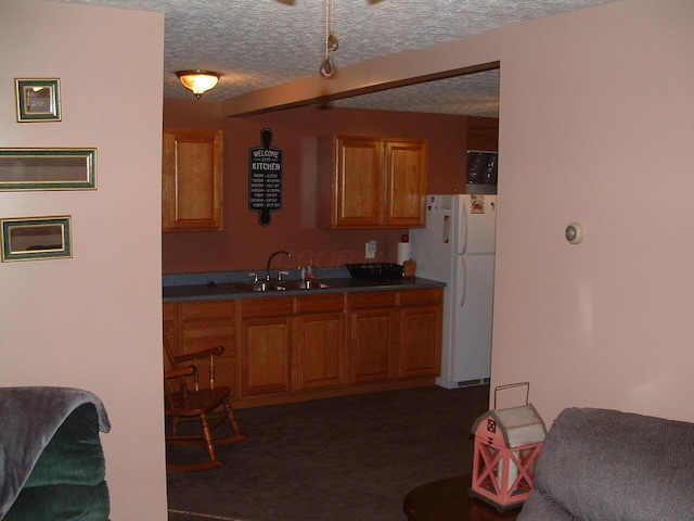 kitchen featuring a textured ceiling, white fridge, sink, and dark colored carpet