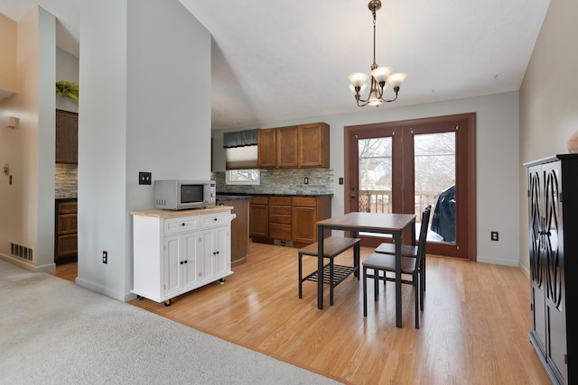 kitchen featuring decorative light fixtures, decorative backsplash, a chandelier, and light wood-type flooring