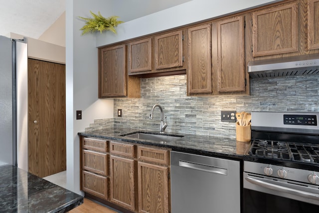 kitchen with sink, appliances with stainless steel finishes, tasteful backsplash, dark stone counters, and wall chimney exhaust hood