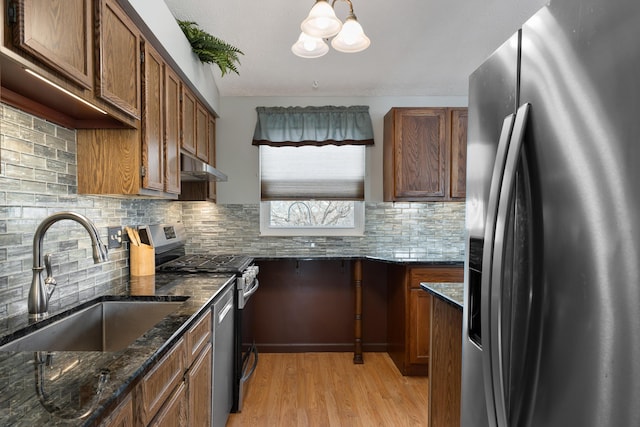 kitchen featuring sink, light hardwood / wood-style flooring, dark stone countertops, pendant lighting, and stainless steel appliances