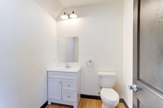 bathroom with hardwood / wood-style floors, vanity, toilet, and lofted ceiling